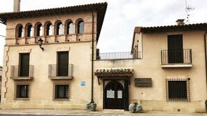 Un edificio con fachada color beige, varias ventanas y una entrada central con un letrero.