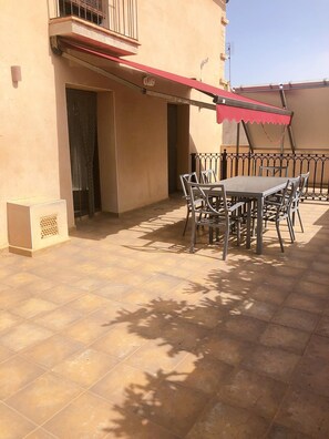Un patio con mesa y sillas, un toldo rojo y una barandilla de metal.