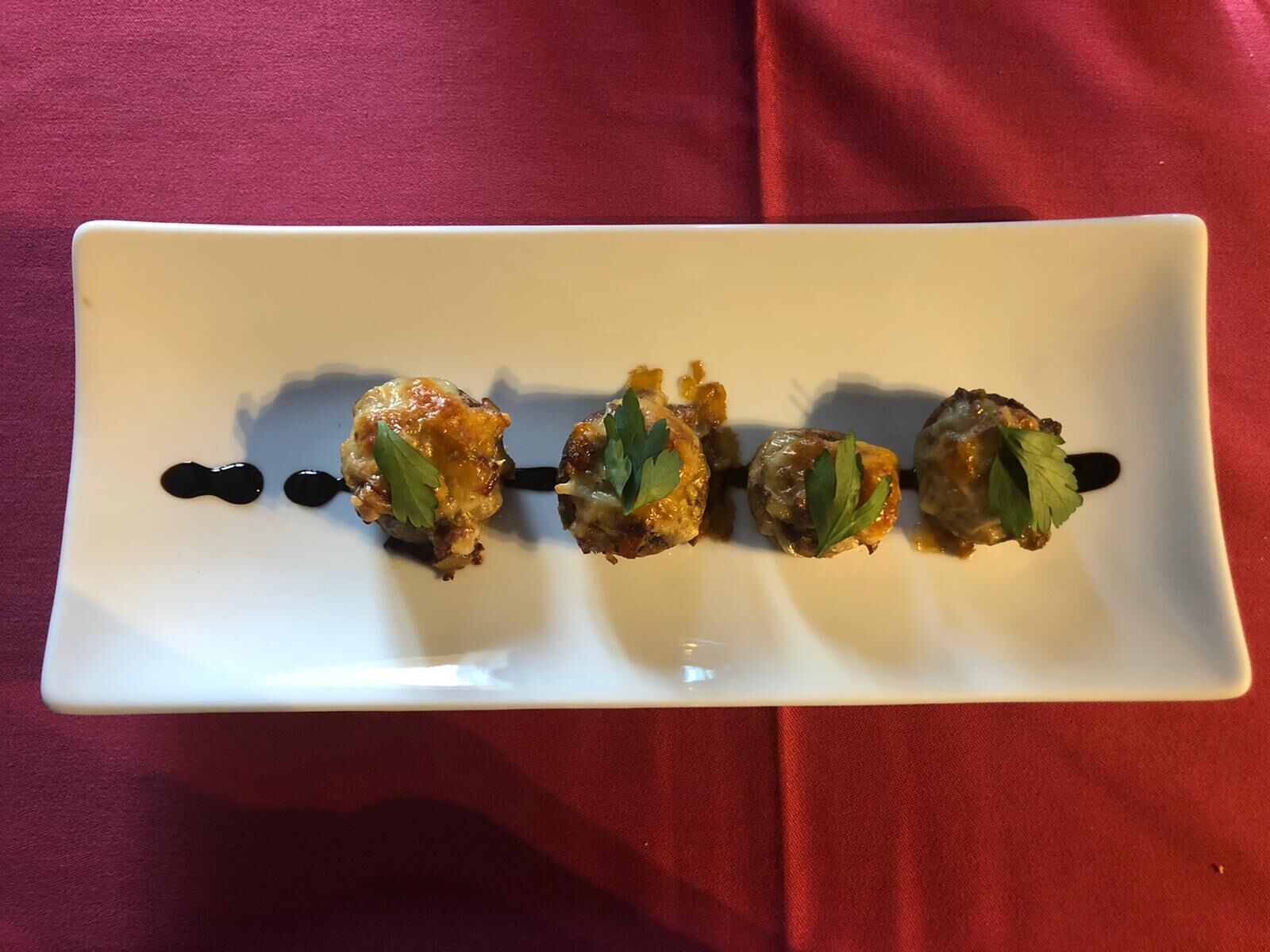 A rectangular white plate with three skewers of food on a red cloth background.