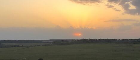A sunset over a rural landscape with a wooden fence in the foreground.