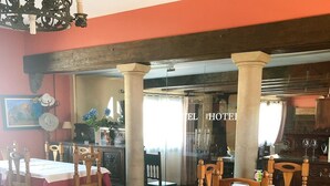 Un comedor de hotel con mesas y sillas de madera, una araña y vistas hacia la entrada del hotel.