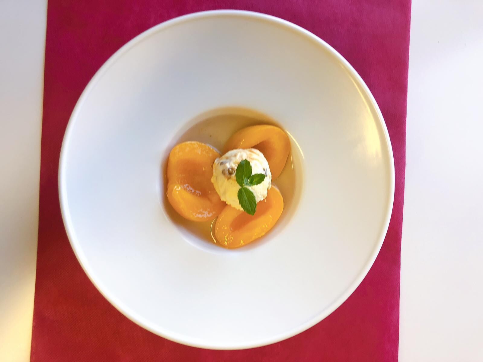 A white plate with sliced peaches and a scoop of ice cream on a red background.