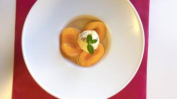 Ein weißer Teller mit Pfirsichspalten und einer Kugel Eis vor rotem Hintergrund.