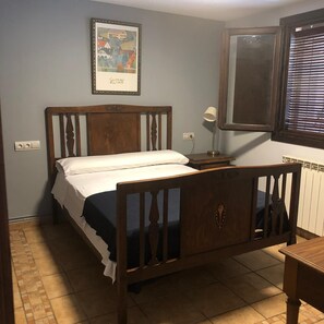 Un dormitorio con una cama de madera, una mesita de noche con lámpara, un cuadro en la pared y una ventana con persianas.