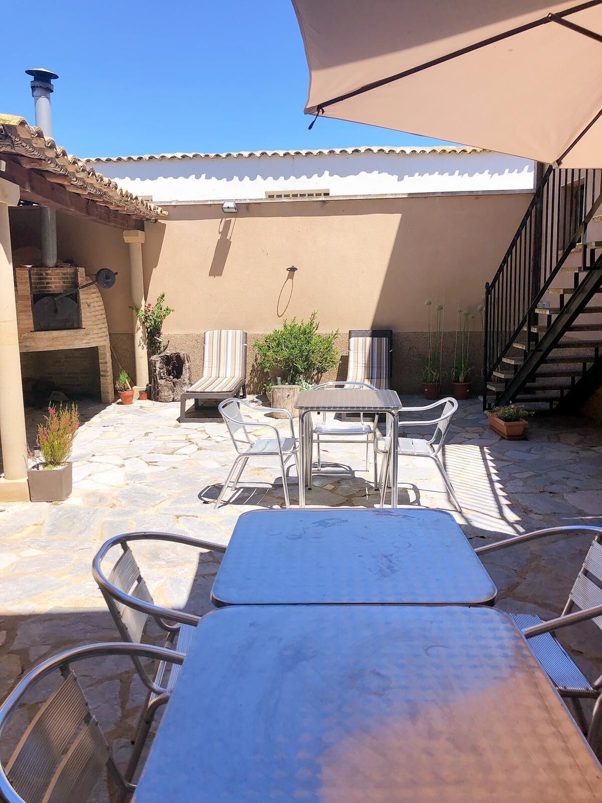 Un patio al aire libre con suelo de piedra, sillas de metal, una mesa, una parrilla y una escalera.