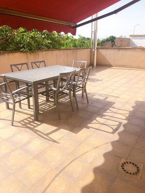Un patio al aire libre con una mesa, sillas, un toldo rojo y suelo de baldosas.