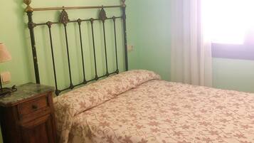 Une chambre à coucher comprenant un lit, une table de chevet, une commode, un climatiseur et une fenêtre avec des rideaux.