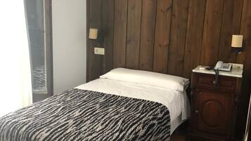 A bedroom with a bed, wooden panel walls, a nightstand, and a lamp.