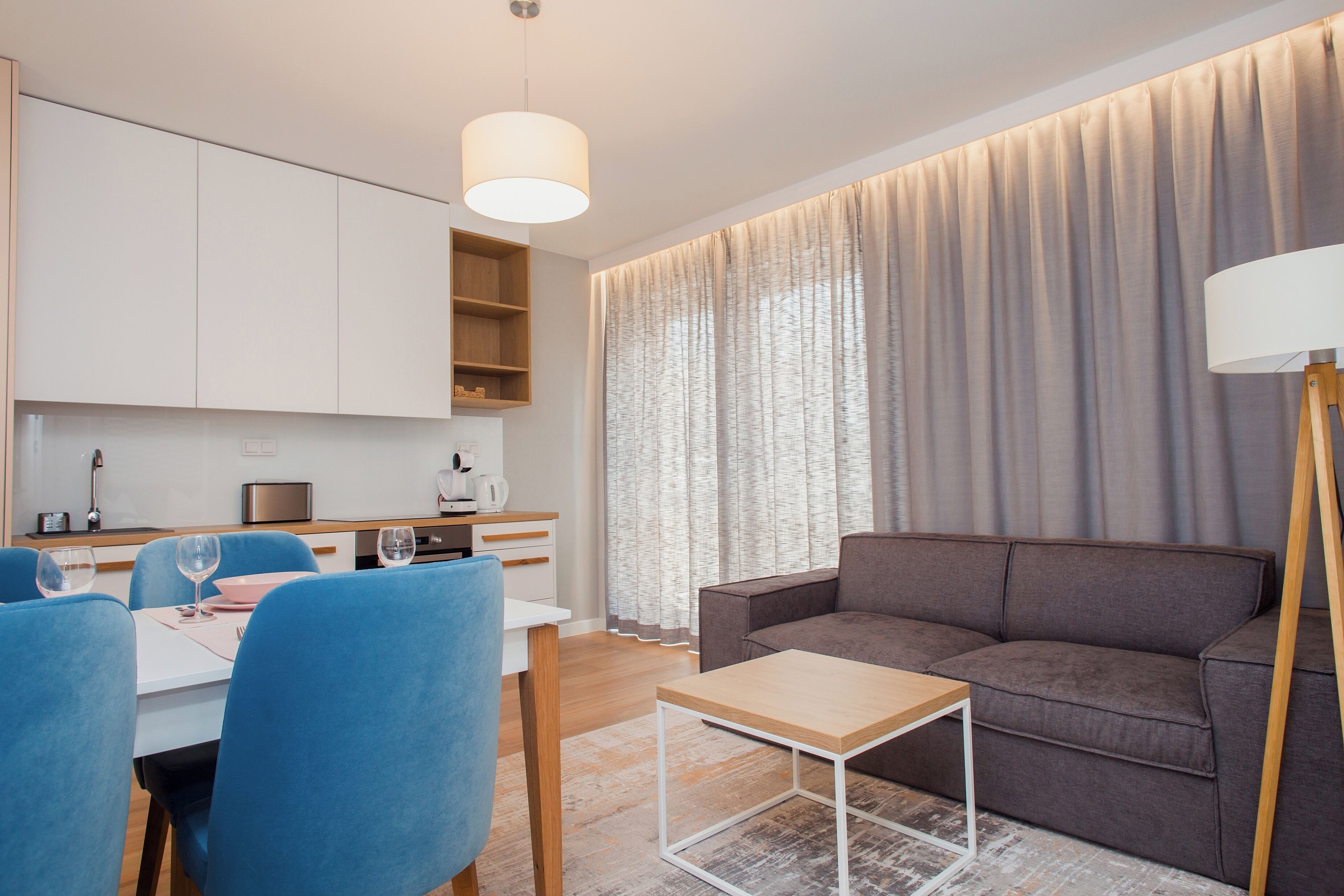 Una sala de estar moderna con un sofá, una mesa de comedor con sillas y una cocina al fondo.