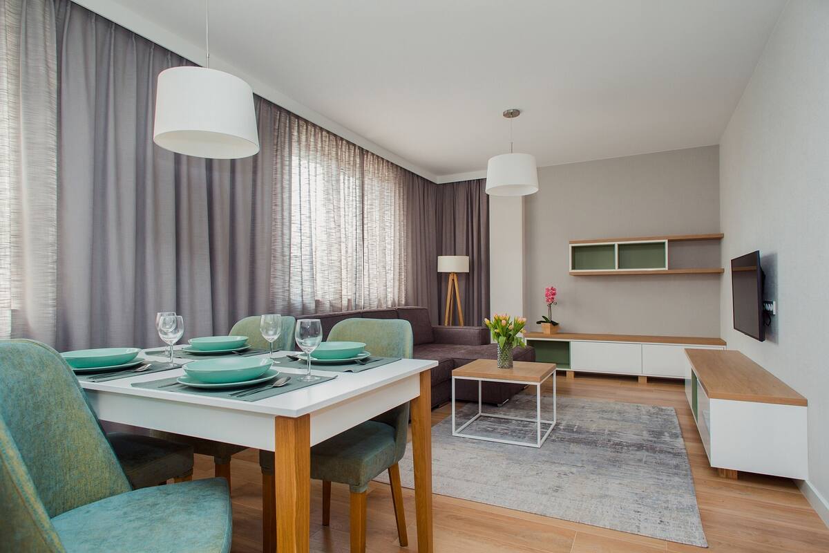A modern living room with a dining area, a sofa, a coffee table, and a TV mounted on the wall.