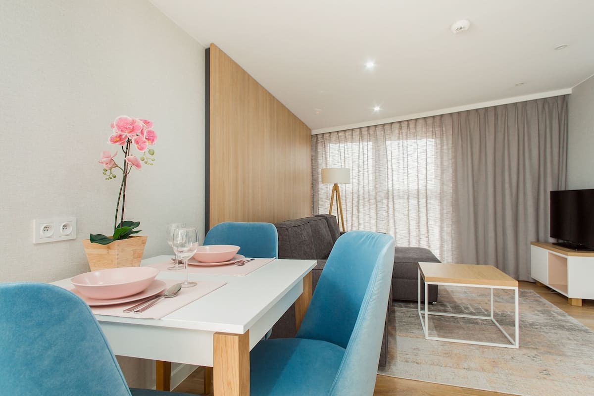 A modern living room with a dining area, a sofa, a TV, and a plant.