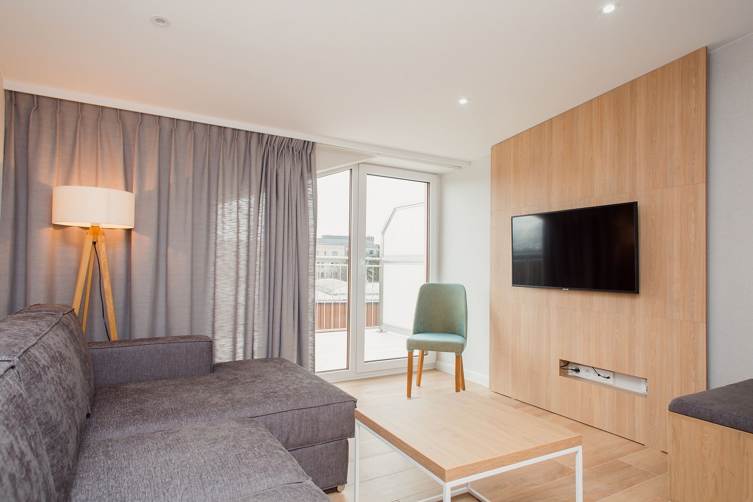 A modern living room with a grey sofa, a wooden coffee table, a green chair, and a flat-screen TV mounted on a wooden wall.