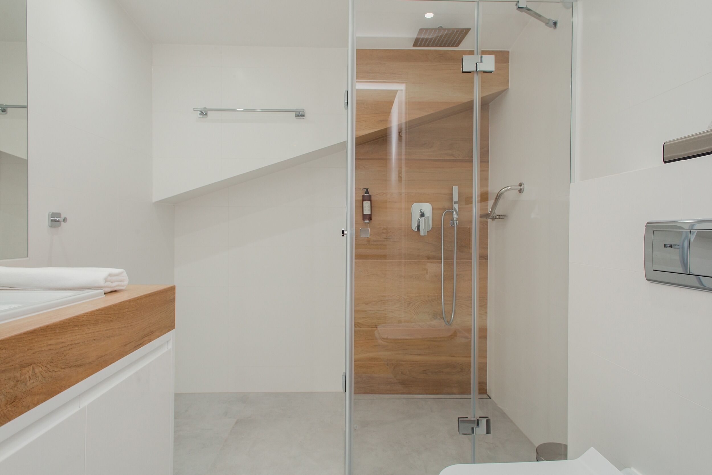 Ein modernes Badezimmer mit Duschkabine aus Glas, einem Holzkosmetikschrank und einem weißen Waschbecken.