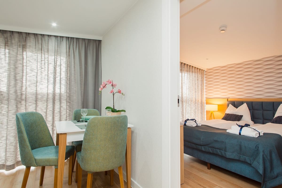 A hotel room with a bed, a dining area with chairs and a table, and a window with curtains.