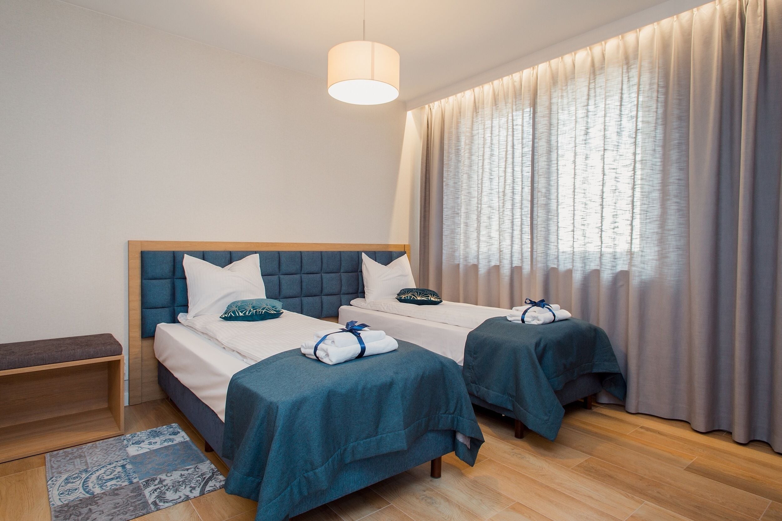 Ein Hotelzimmer mit zwei Betten, einer Bank und einem großen Fenster mit Vorhängen.