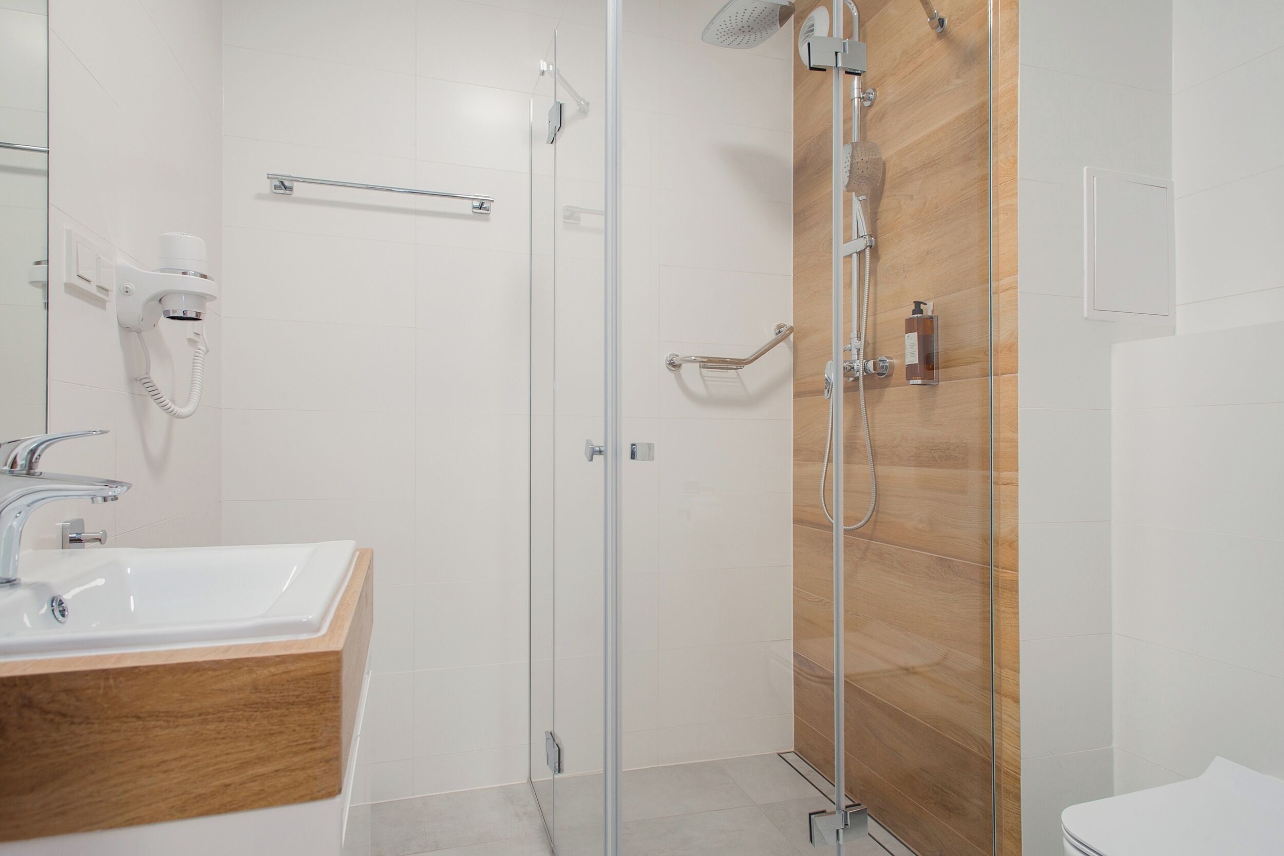 Un baño moderno con ducha de vidrio, tocador de madera y un inodoro blanco.