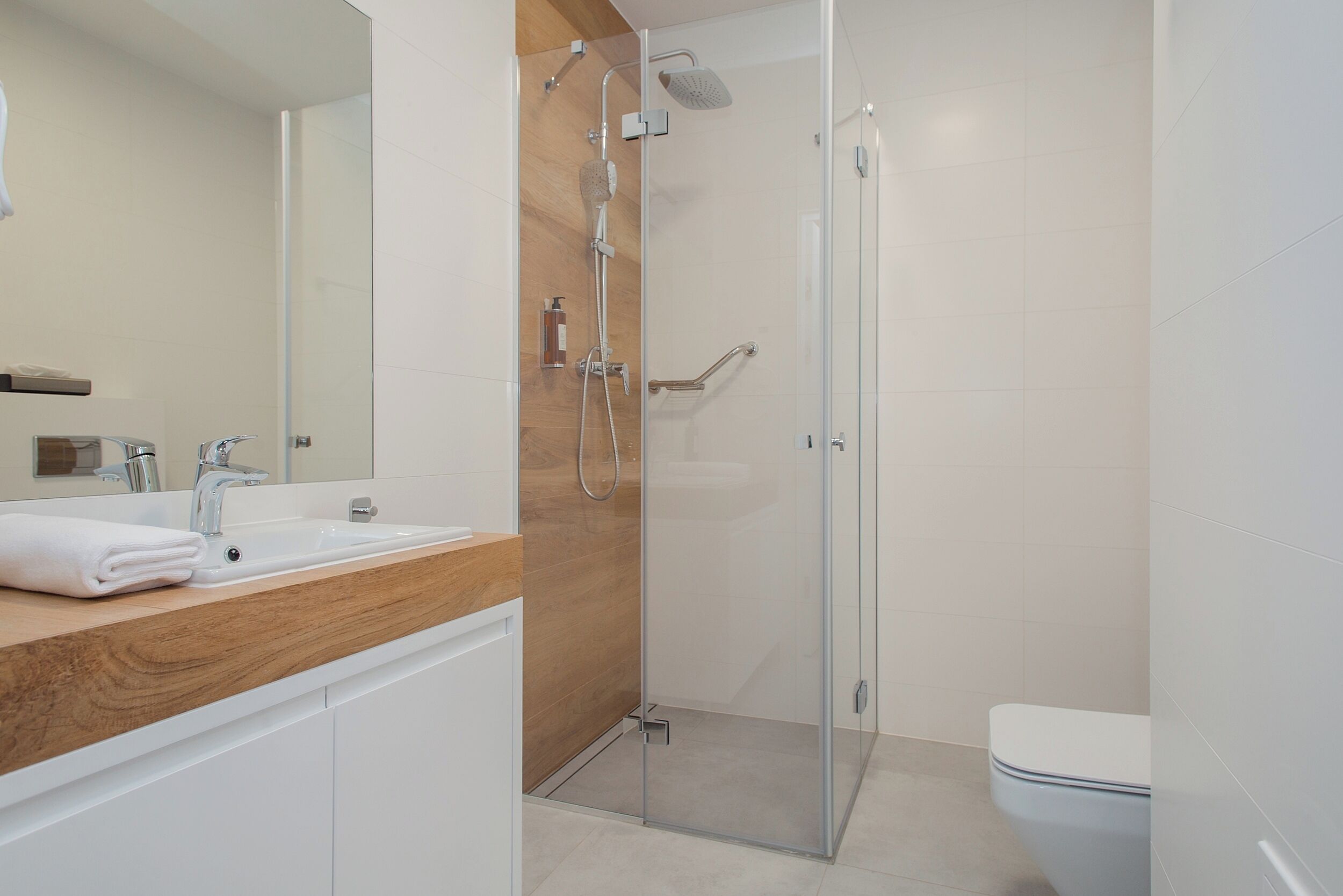 A modern bathroom with a glass-enclosed shower, a wooden vanity, and a white toilet.