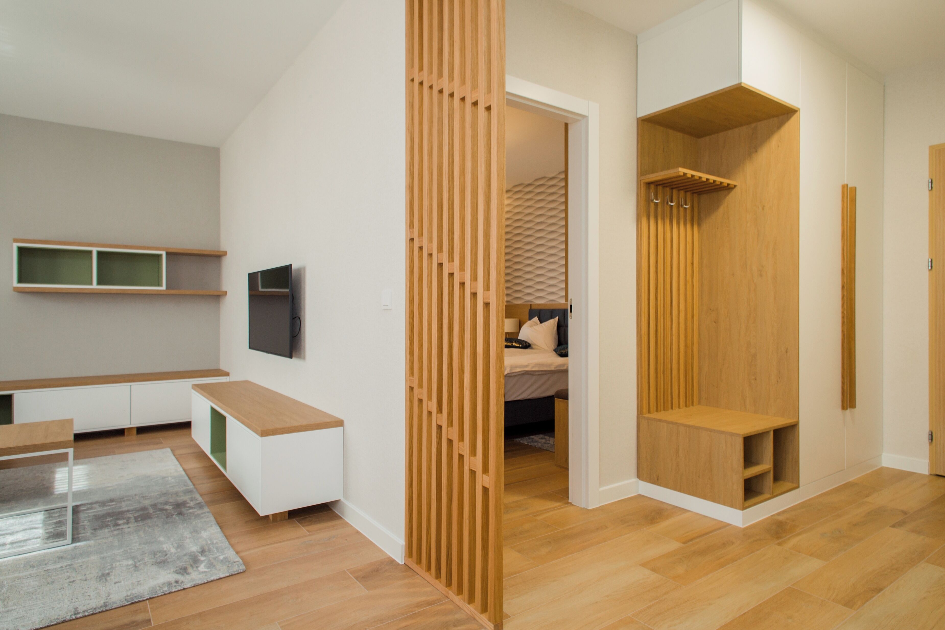 Un interior moderno con un banco de madera, un televisor montado en la pared y una cama con cabecera estampada.