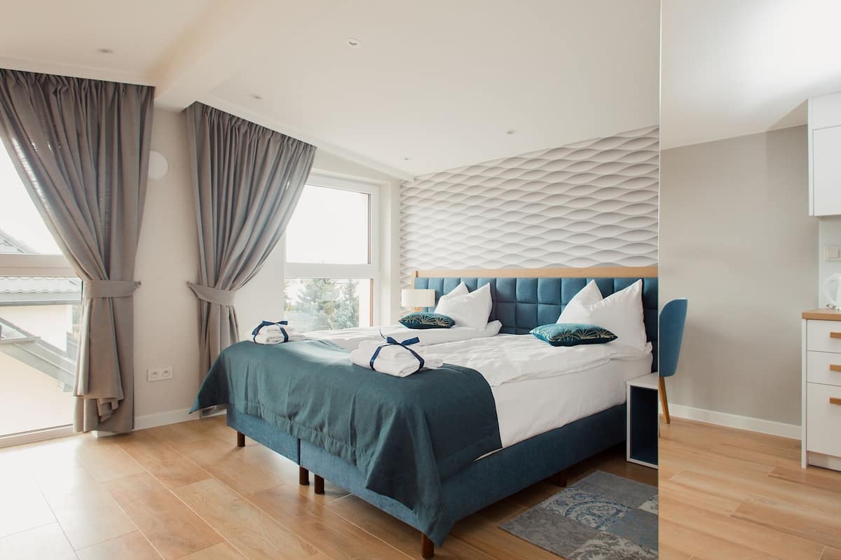A modern bedroom with a large bed, a headboard with a textured pattern, and a view of the outdoors through a large window.