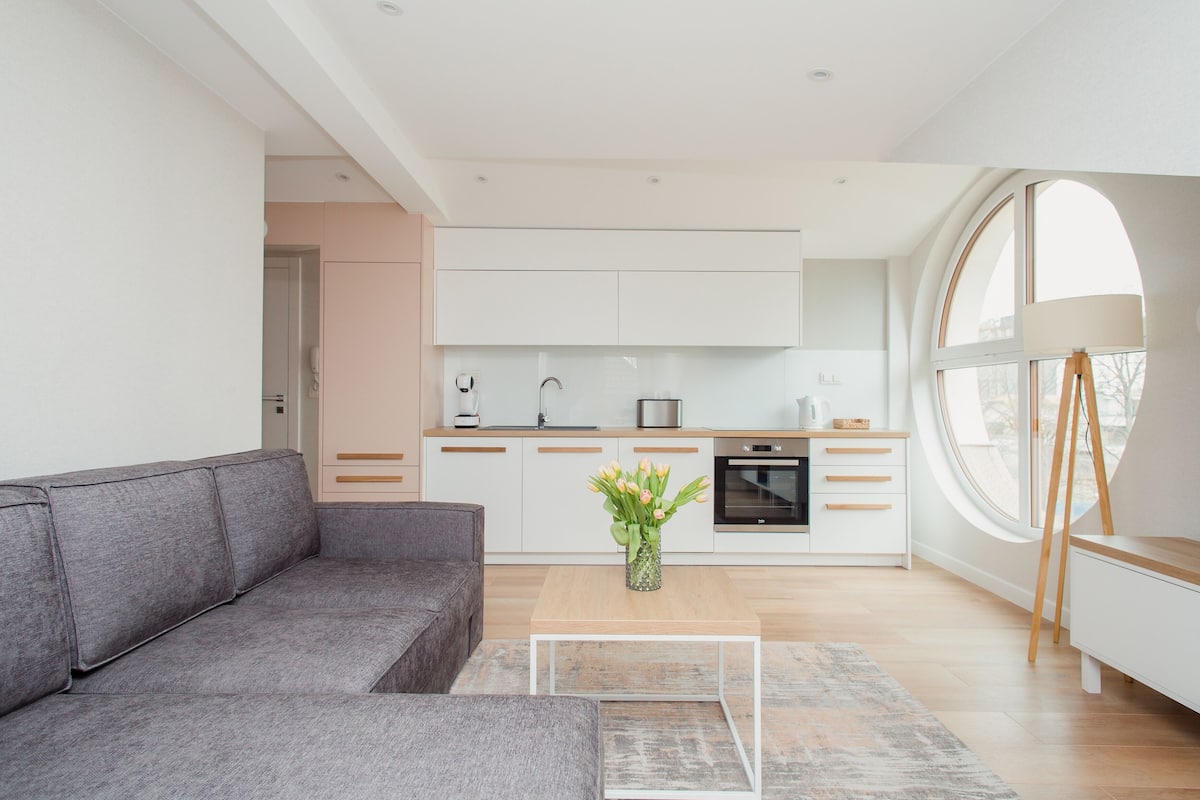 A modern living room with a grey sofa, a coffee table, and a kitchen in the background.