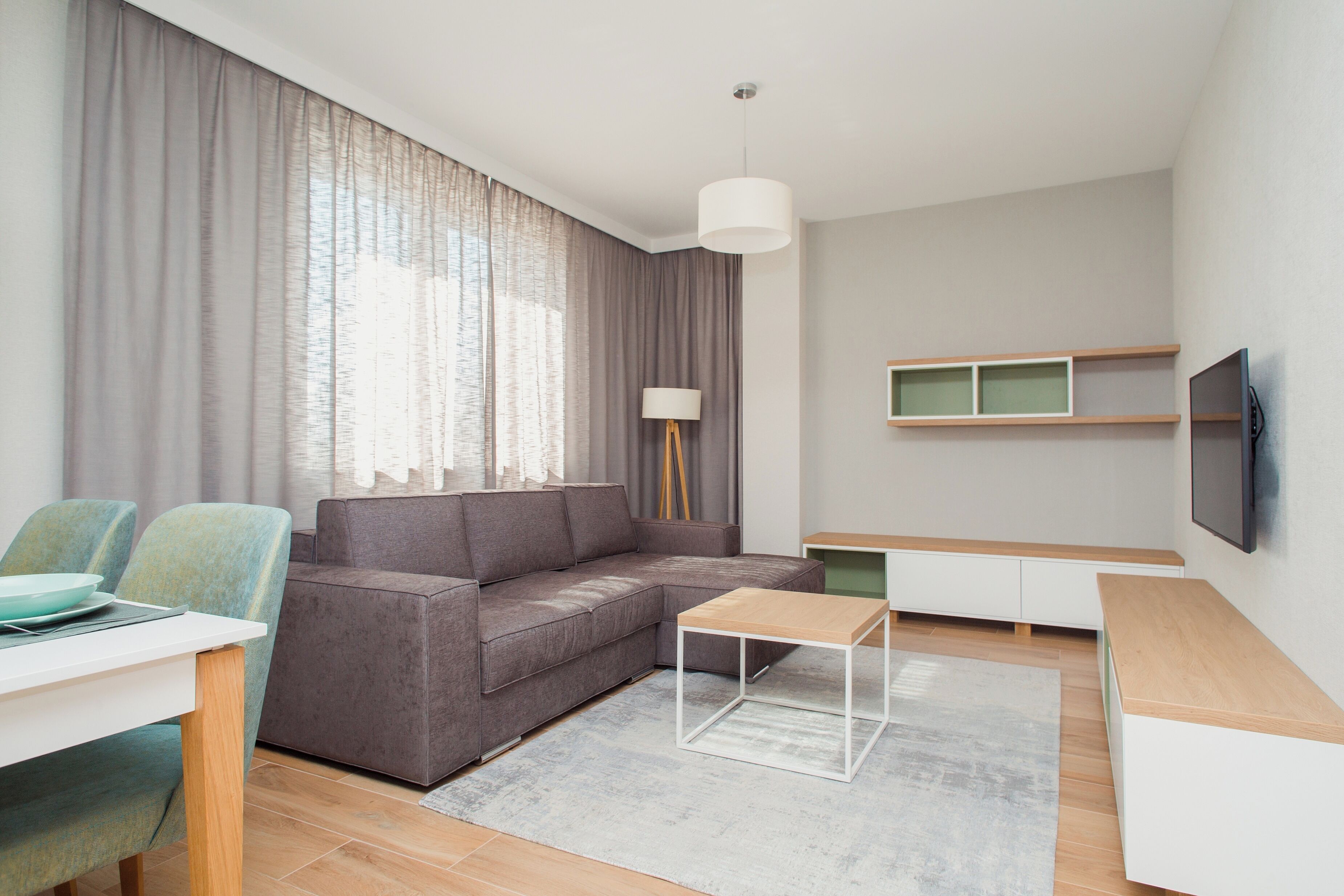 A modern living room with a grey sofa, a small wooden coffee table, a white TV stand, and a dining area with a table and chairs.