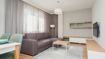 A modern living room with a grey sofa, a small wooden coffee table, a white TV stand, and a dining area with a table and chairs.
