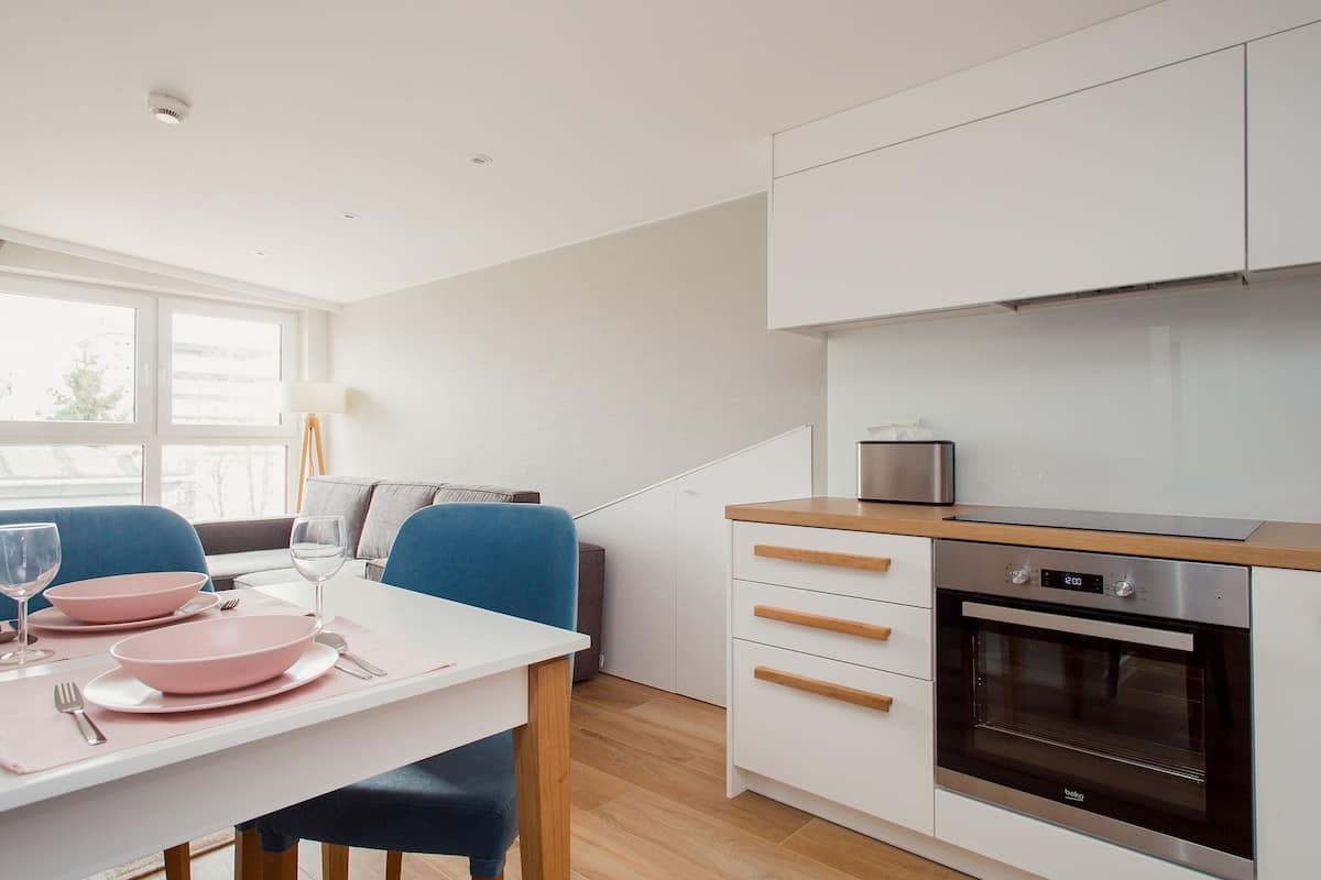 A modern kitchen with white cabinets, a stainless steel oven, and a dining area with a white table and blue chairs.