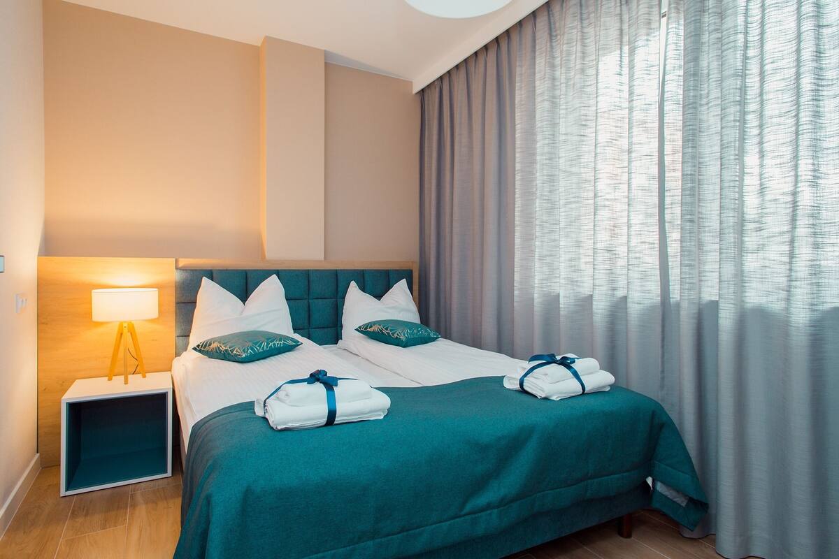 A hotel room with a bed, a nightstand, a lamp, and a window with curtains.