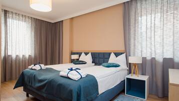A hotel room with a large bed, a bedside table with a lamp, and a view of the outside through curtains.