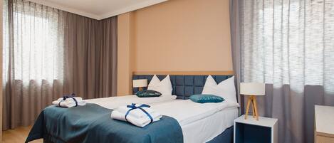 Habitación de hotel con una cama grande, una mesita de noche con lámpara y vistas al exterior a través de cortinas.