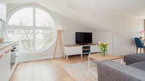 A modern living room with a large window, a flat-screen TV, a wooden coffee table, and a grey sofa.