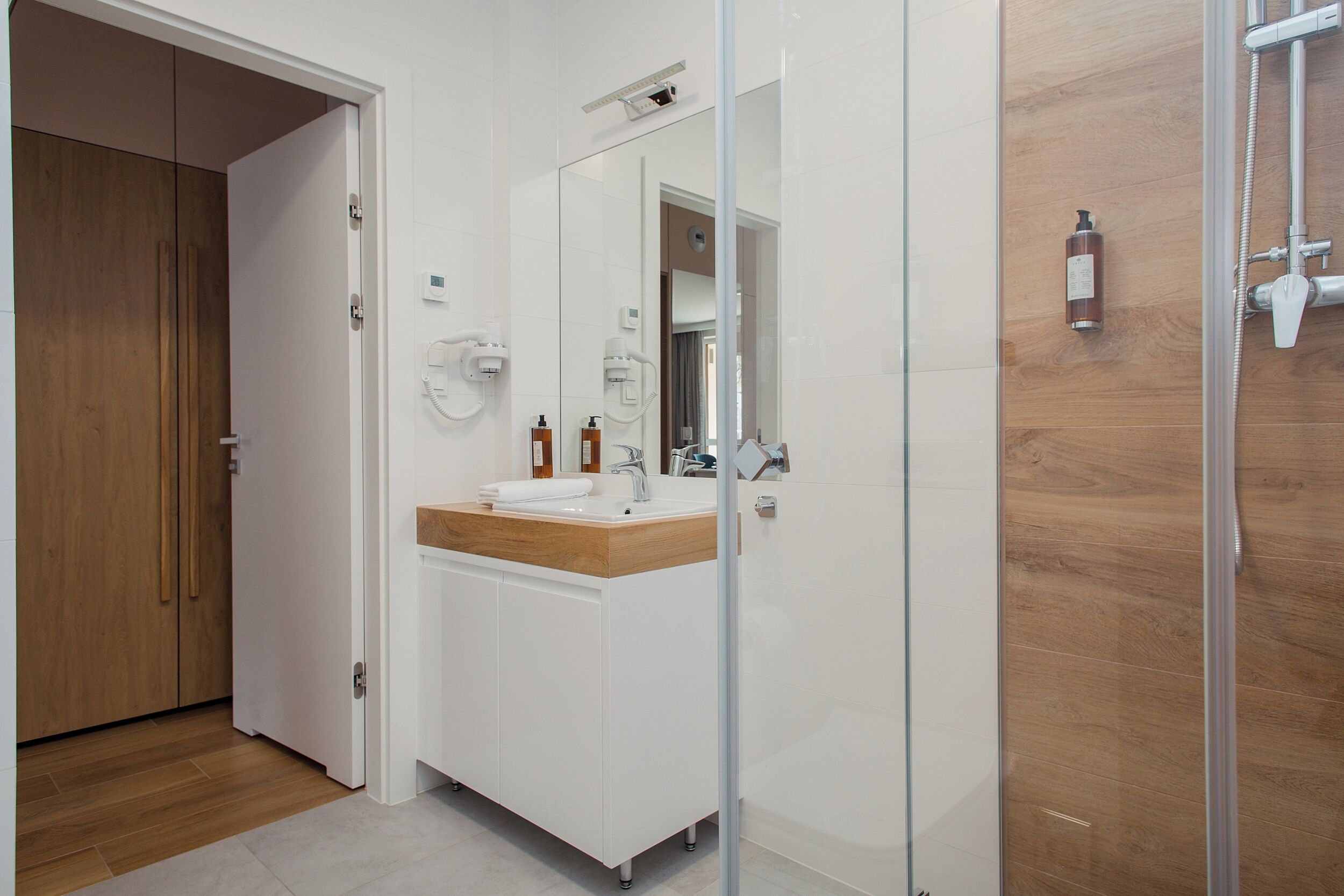 Un baño moderno con tocador de madera, cabina de ducha de vidrio y lavamanos blanco.