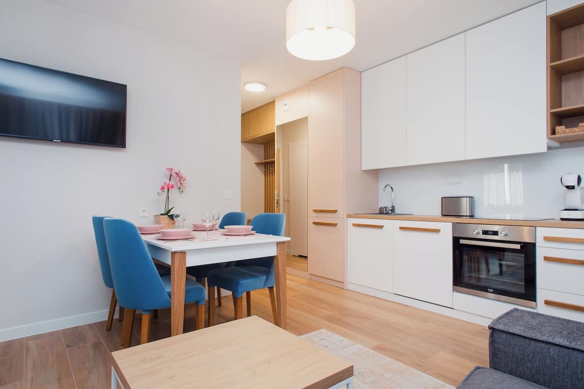 A modern kitchen with white cabinets, a built-in oven, and a dining area with a white table and blue chairs.