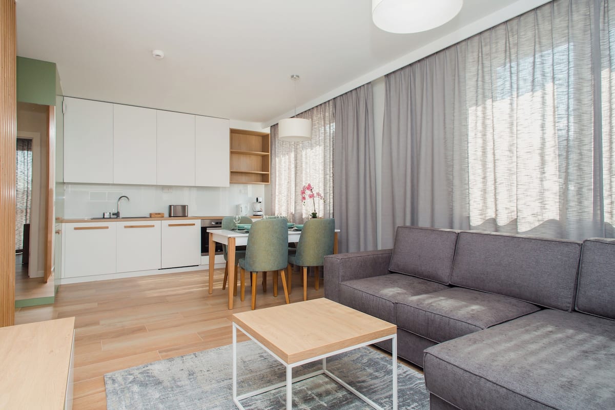 A modern living room with a grey sofa, wooden coffee table, and a dining area with chairs and a table.