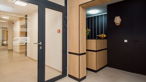 A modern hotel lobby with a glass door, wooden paneling, and a black wall with a decorative light fixture.