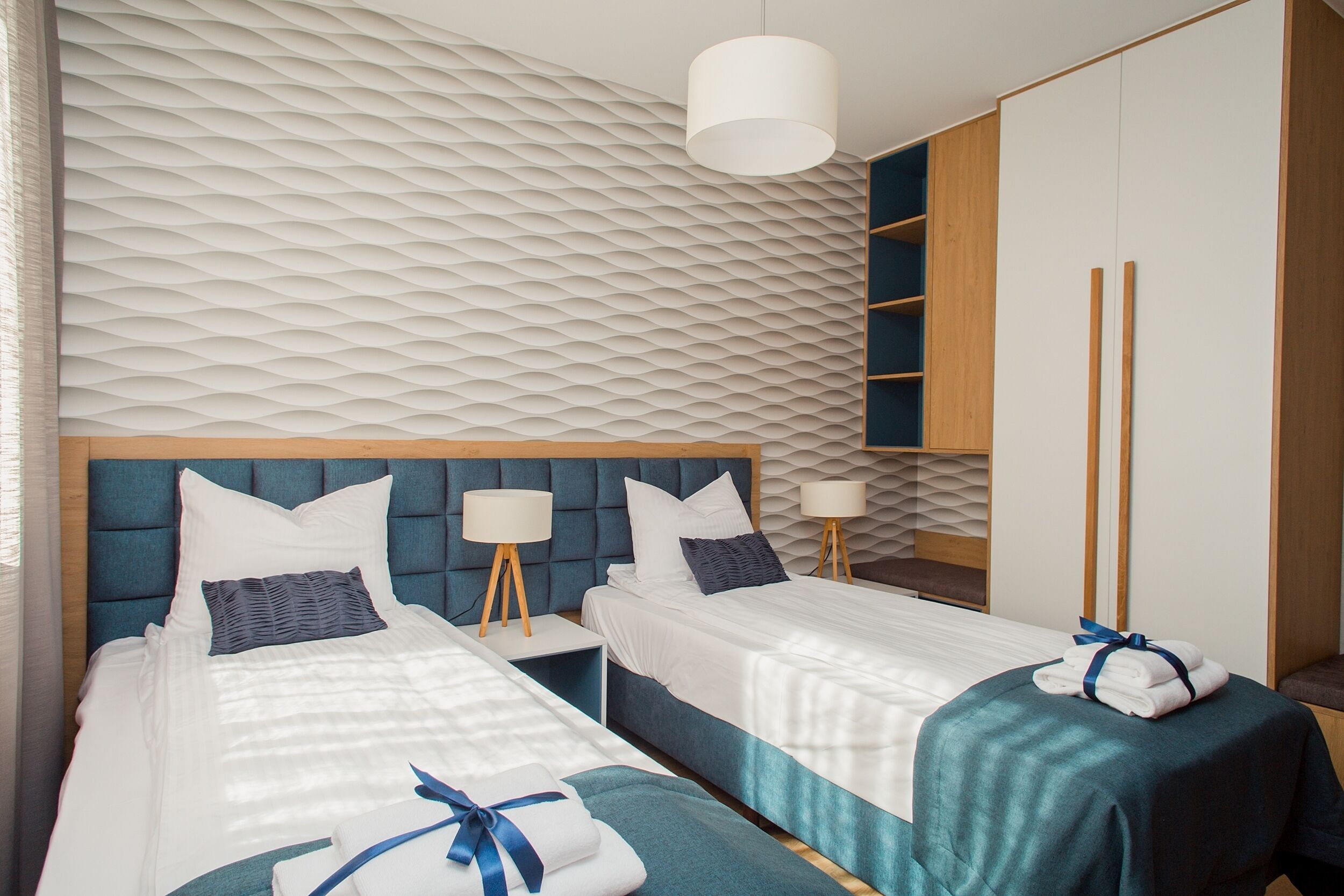 A hotel room with two beds, a wardrobe, and a textured wall.