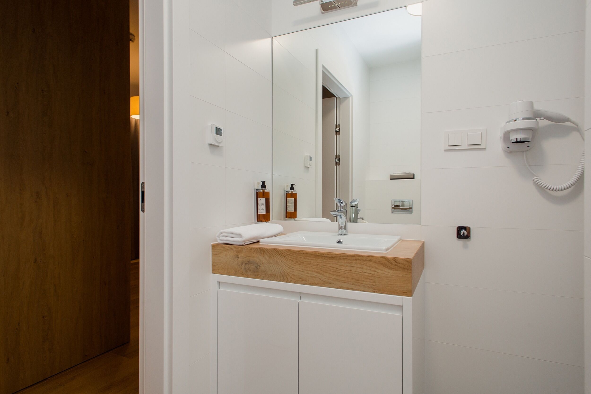 A modern bathroom with a wooden vanity, a large mirror, a hairdryer, and a towel on the counter.