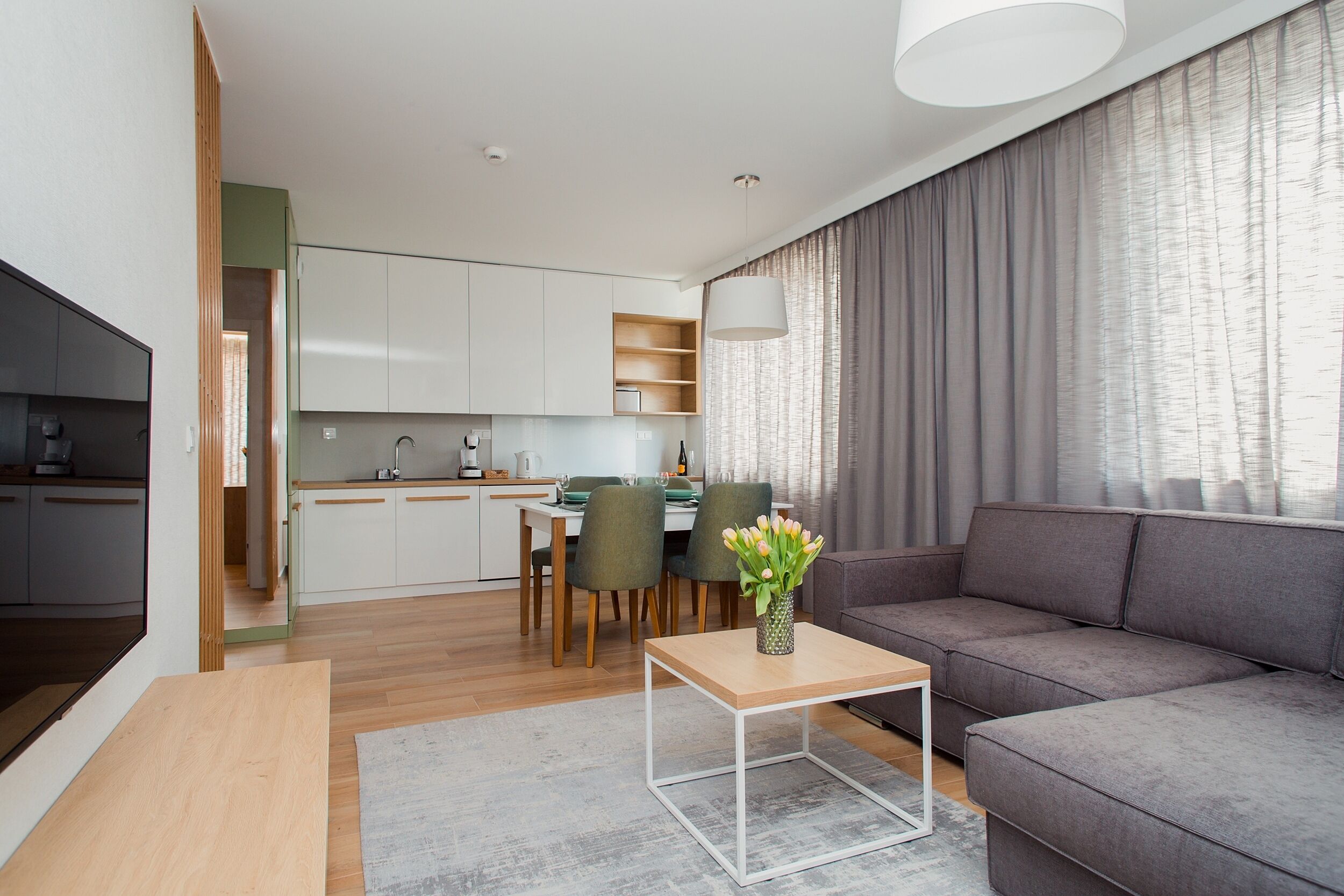 Un salon moderne avec un canapé gris, une table basse en bois et un coin repas comprenant une table et des chaises.