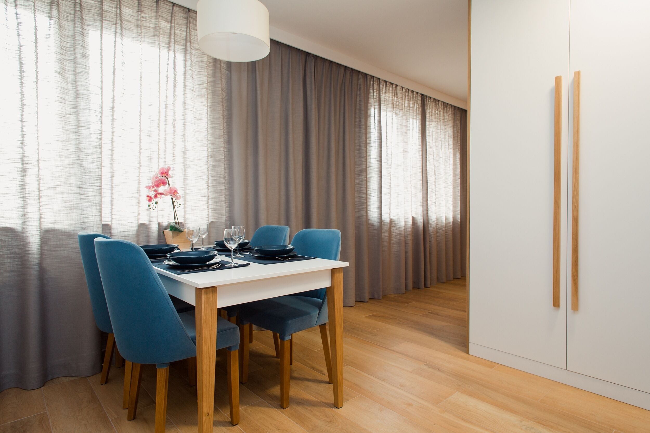 Un espace repas moderne avec une table blanche, des chaises bleues et un vase rempli de fleurs roses.
