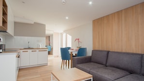 A modern living room with a grey sofa, a wooden coffee table, and a dining area with blue chairs.