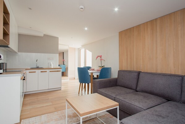 Una sala moderna con un sofá gris, una mesa de centro de madera y un comedor con sillas azules.