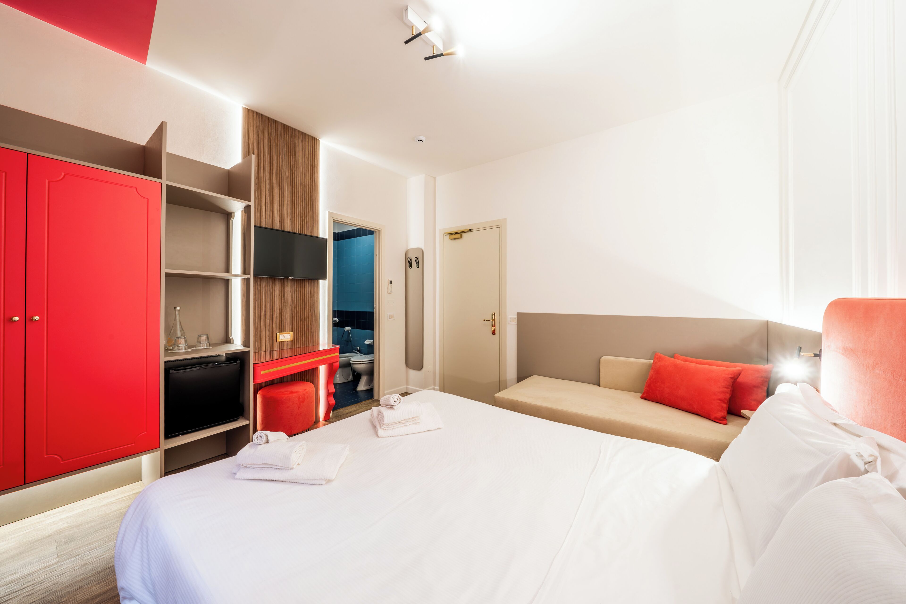 A hotel room with a bed, a red wardrobe, a TV, a desk, and a sofa.