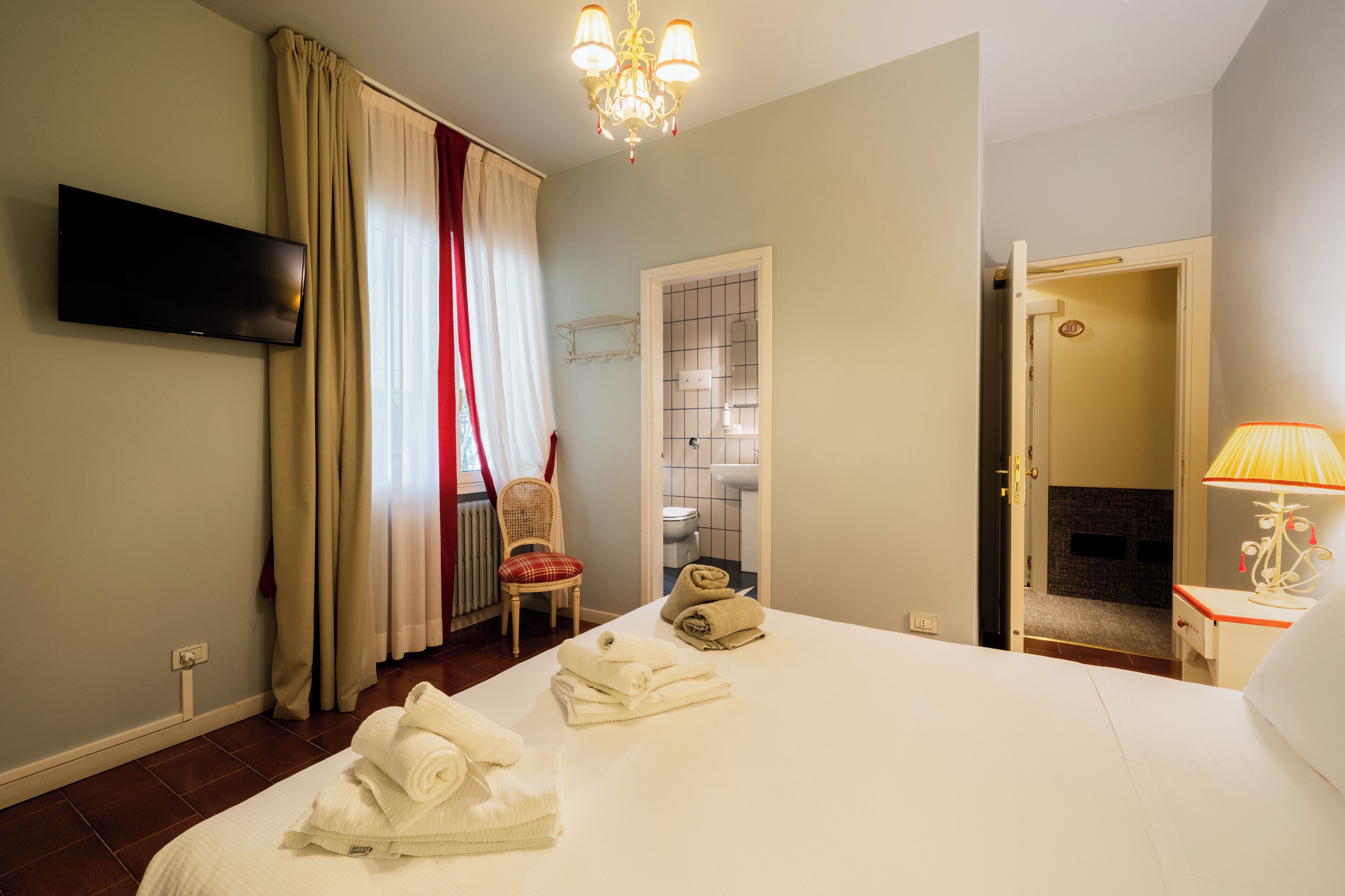 Une chambre d’hôtel comprenant un lit, une télévision, une chaise, une salle de bain et une porte donnant sur une autre pièce.