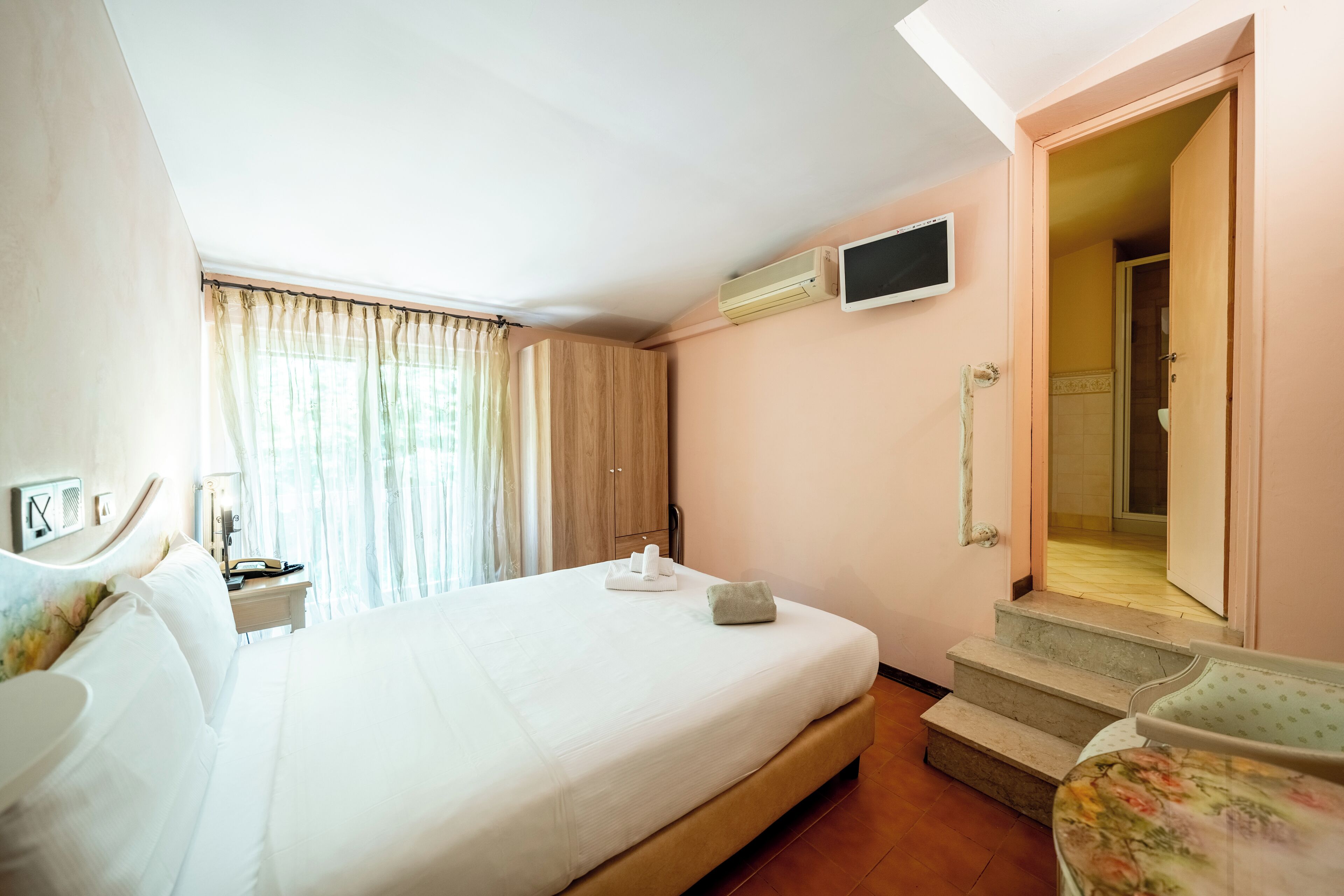 A hotel room with a bed, a TV mounted on the wall, a bathroom door, and a staircase leading to the bathroom.