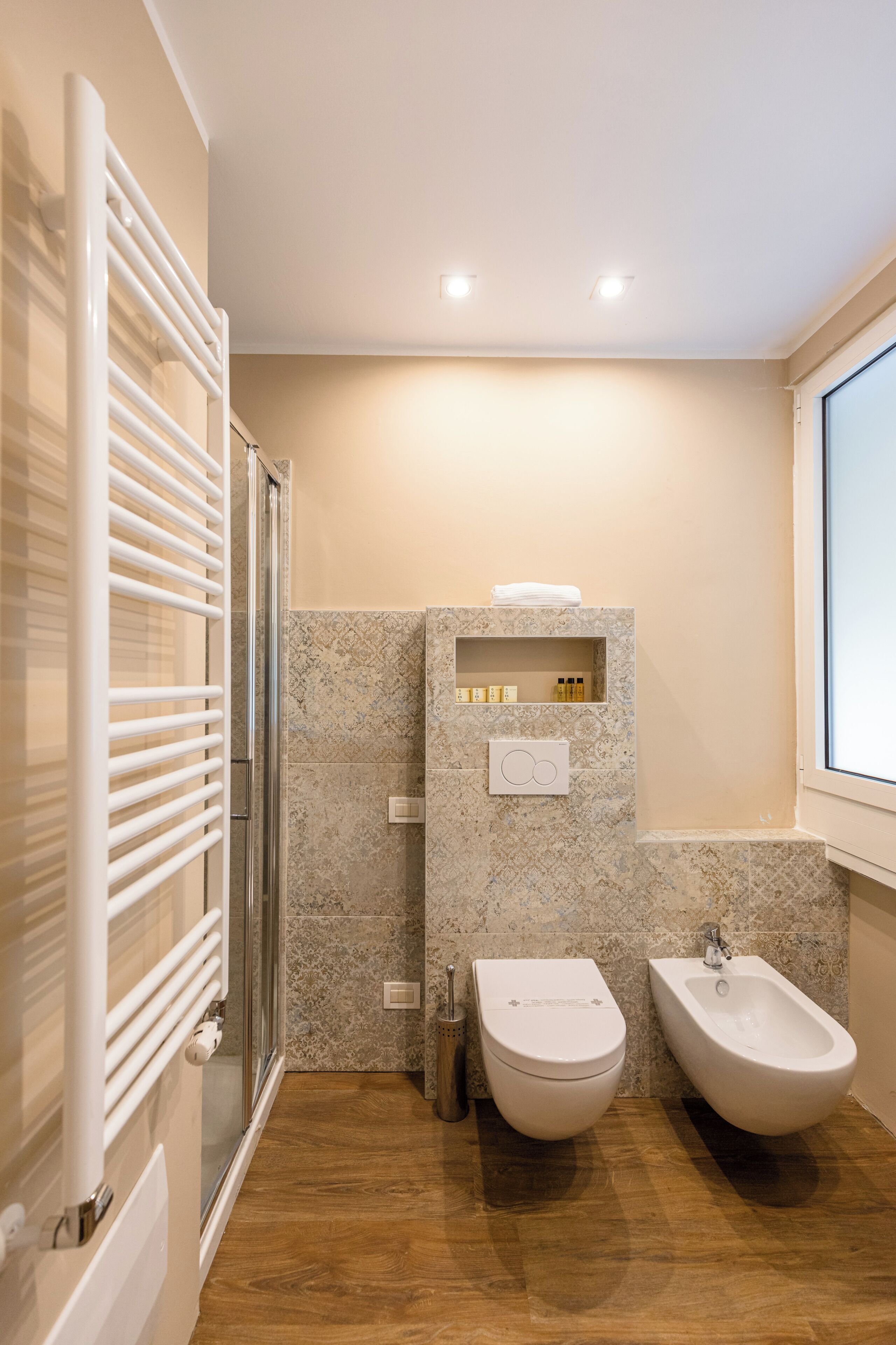 A bathroom with a shower, toilet, bidet, and a shelf with toiletries.