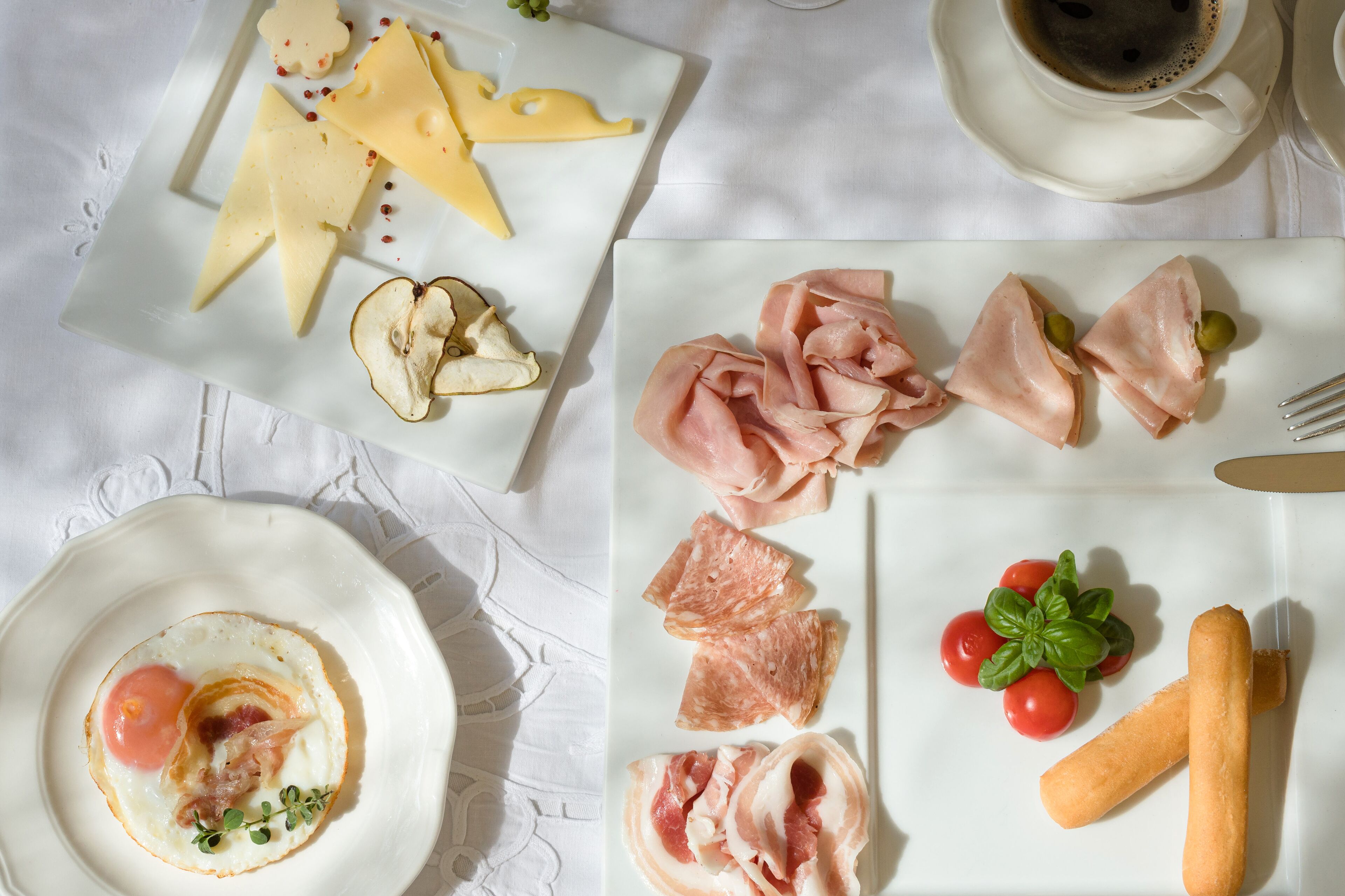 Een ontbijttafel met diverse etenswaren, zoals kaas, ham, tomaten en brood.