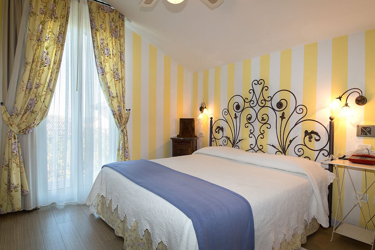 A hotel room with a bed, curtains, a nightstand, and a wall-mounted lamp.