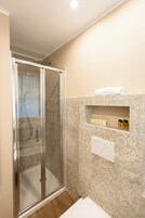Un baño con ducha de vidrio, lavamanos blanco y pared de mármol.