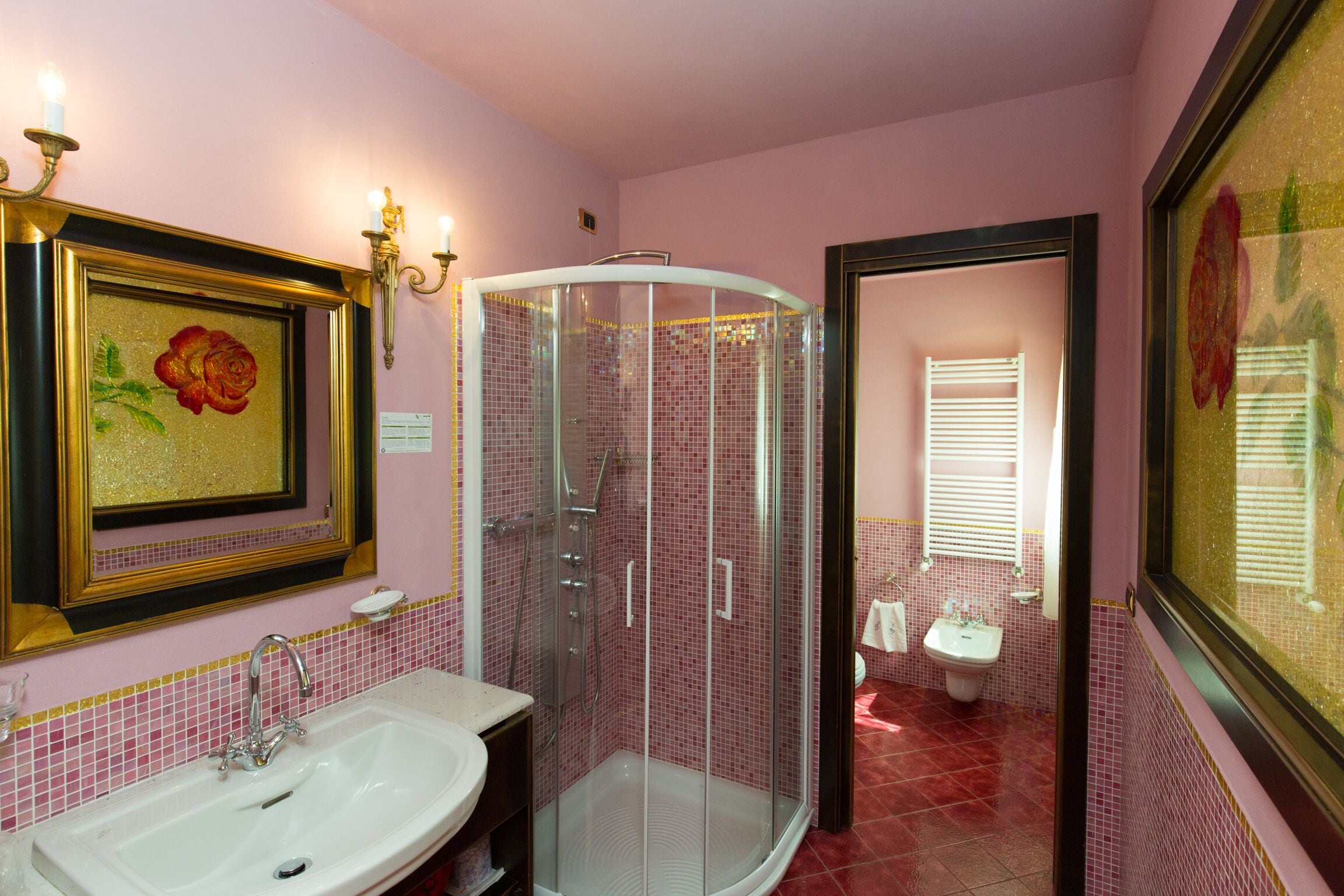 A bathroom with a glass-enclosed shower, a sink, and a mirror with a framed picture.