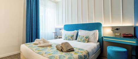 A hotel room with a bed, a desk, a chair, a nightstand, and a window with curtains.